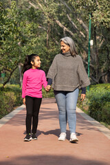 Fototapeta premium Happy grandmother holding grandkids hands and walking in park