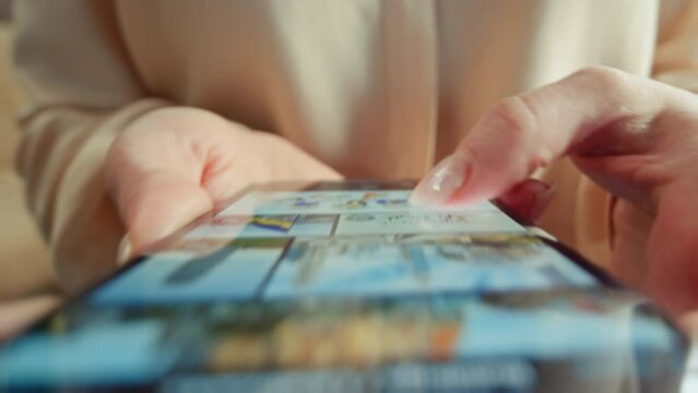 Unrecognizable woman choosing online games in app store on smartphone. Close-up shot of girl in blouse using game platform on device. Female hands touching screen of mobile phone, scrolling