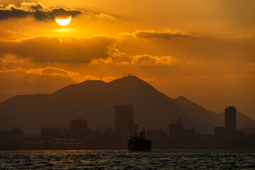 Fototapeta premium 関門海峡の夕日が照らす皿倉山と小倉の街影を背に船影を見る20231226