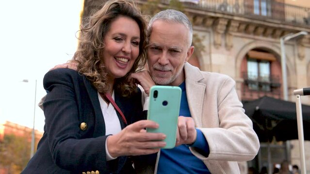 Cheerful mid adult couple having fun together taking a selfie in the street. Romantic senior couple smiling taking picture together in european city.
