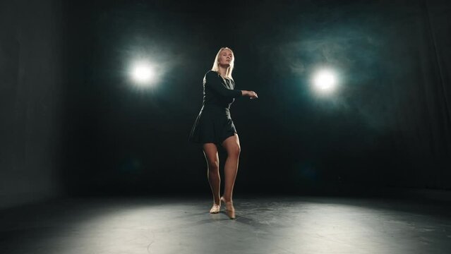 Woman choreographer dancing jumping. Blonde hard-working female ballerina dances in black dress in studio on stage. Performing dance element classical ballet bouncing in air. Classical choreography.