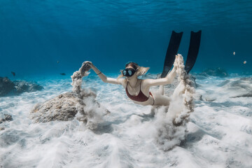 Free diver swims underwater and playing with sand. Freediving with attractive woman in tropical...