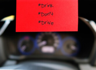Red stick note with text written DRINK DON'T DRIVE  on the car steering wheel , to remind driver to...