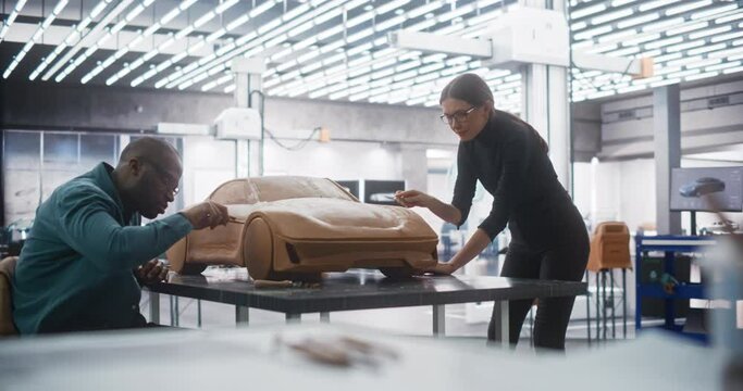 Young Female Apprentice Car Modeler Working with Black Senior Automotive Designer on Creating a 3D Polymer Clay Model of a Modern Electric Car. Team of Diverse Specialists Working in Creative Agency