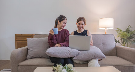 Two women communicate with friends and classmates via video link using laptop and smartphone in living room. Friends, friendship, time together.