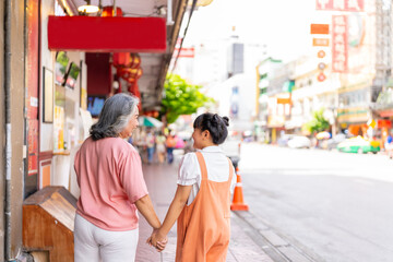 Happy Asian family grandmother and grandchild girl walking and shopping together at street market. Senior woman and little girl enjoy and fun outdoor lifestyle travel in the city on summer vacation.