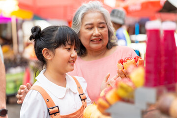 Happy Asian family grandmother and grandchild girl buying and drinking fruit juice together at...