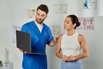 Fototapeta premium handsome bearded doctor and his young patient looking at laptop during appointment, healthcare