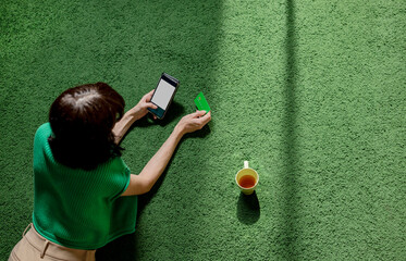 Woman lying on carpet and using credit card for online shopping through smart phone at home