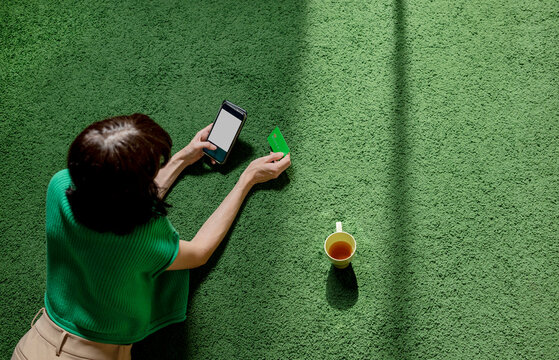 Woman lying on carpet and using credit card for online shopping through smart phone at home