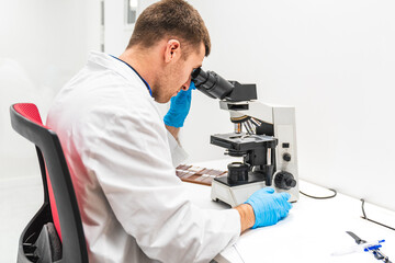 Naklejka na ściany i meble Concentrated male lab technician in white coat analyzing tissue samples through a microscope in a clinical hospital setting.