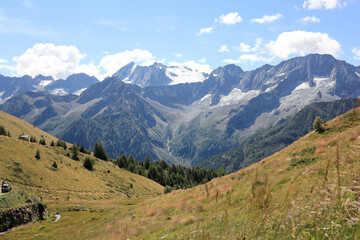 Landscape with fields, glacier and mountains in the Italian Alps, under a brilliant sunny an cluody sky