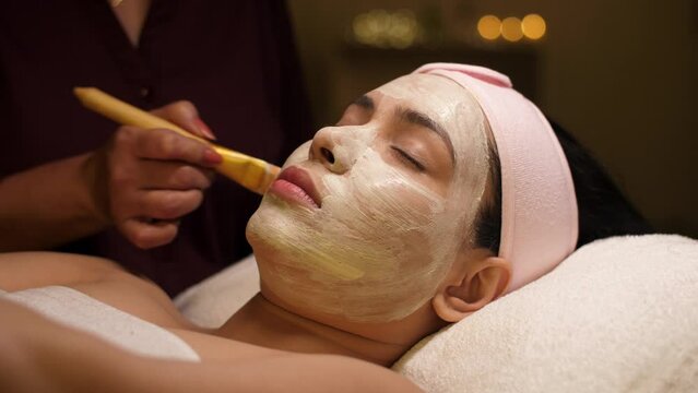 Applying avocado face mask with a brush - spa treatment  relaxing routine  detoxification  break from routine  acne treatment. A beautiful lady getting a face pack on her face with a brush - face c...