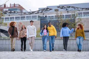 Group of six friends striding forward in an urban landscape, showing unity and confidence with...