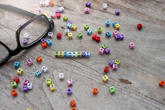 The word "BREAKOUT" is on the wooden table. Eyeglasses are at the side and colorful cubes are scattered around on the wooden table.