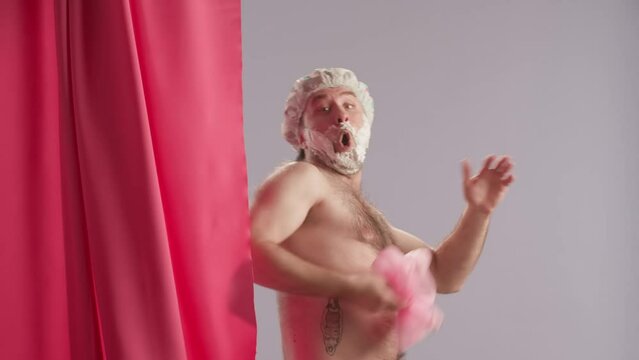 Silhouette of a washing man behind a pink shower curtain. The curtain opens, the man with shaving foam on his face shrieks, throws the washcloth, closes the curtain, wraps his arms around himself.
