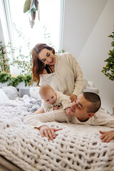 Happy family with one baby spending time at home. Parents playing with their baby on bed.