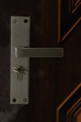 A silver colored door handle or door knob on a brown door or gate 
