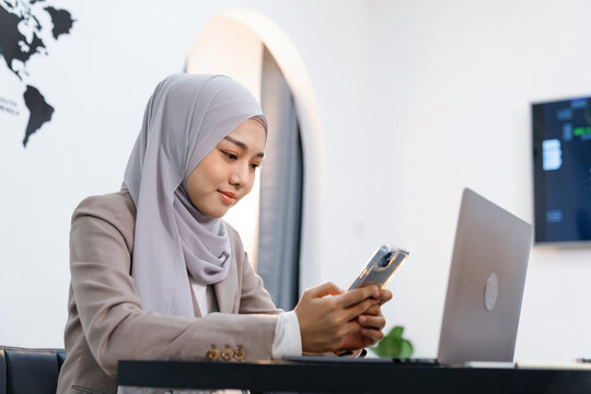 Beautiful Muslim woman talking on the phone and using a computer on her desk. 