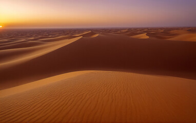 Sunset over a desert with sand dunes and purple-yellow sky.