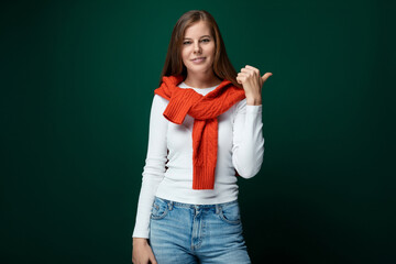 Positive young woman tied a red sweater over her shoulders and points her hand to the side