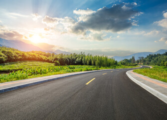 Country road and green forest with mountain nature landscape at sunset - obrazy, fototapety, plakaty