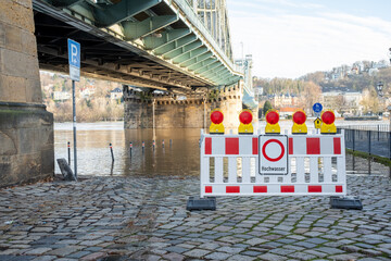 A full river that has burst its banks, and in the foreground is a stop sign with the words Hochwasser (flood). High water in Dresden. Overflowed river bank and cycle path. Flood warning level 3