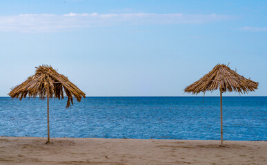 Fototapeta na wymiar two straw beach umbrellas on an empty seashore on a clear day