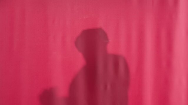 Silhouette of a washing man behind a pink shower curtain. Behind pulled back curtain a man is washing himself and dancing vigorously. Back view of a nude man having fun in the shower.