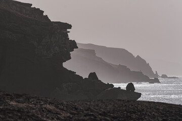 View of the silhouettes of rocks, the ocean and the figure of a fisherman in the distance on the beach La Pared on the Canary island of Fuerteventura, Spain.