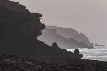Crédence de cuisine en verre imprimé les îles Canaries View of the silhouettes of rocks, the ocean and the figure of a fisherman in the distance on the beach La Pared on the Canary island of Fuerteventura, Spain.