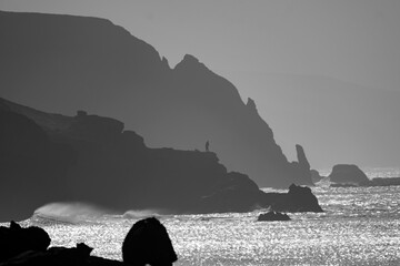 View of the silhouettes of rocks, the ocean and the figure of a fisherman in the distance on the...