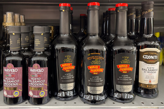 Italy - December 24, 2023: Balsamic Vinegar of Modena in glass bottles of various types and brands displayed on shelf for sale in Italian supermarket