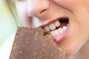A girl bites a chocolate with her teeth in close-up. The harm of sweets for teeth. Addiction of...