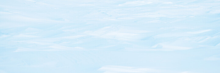 Wide panoramic winter background with snowy ground. Natural snow texture. Wind sculpted patterns on...