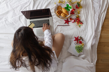 woman sitting in her room is happily shopping for gifts online with her credit card as she prepares for Christmas. woman uses laptop to access an online shopping website and pay with her credit card.