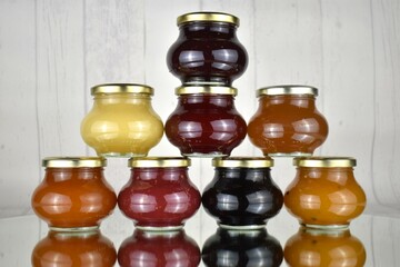 Colorful stacked glasses of jam, preserve, marmelade on mirror with white background 