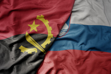 big waving national colorful flag of slovenia and national flag of angola .
