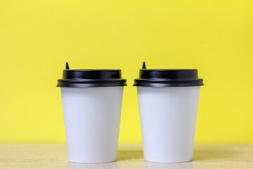 Paper cups for takeaway coffee on a light yellow background.