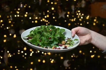 Teller mit Feldsalat, Granatapfel und Walnüssen als Weihnachtsessen an Weihnachten vor Weihnachtsbaum mit Lichtern