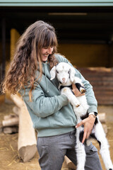 Happy young farmer woman hugging a baby goat on a rural organic farm. Animal welfare and care in a barn.