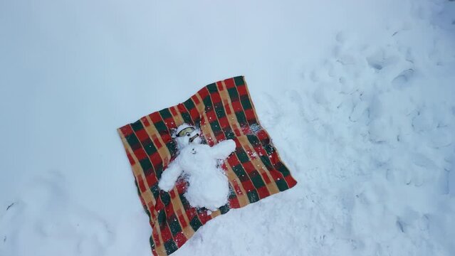 snowman lying with arms outstretched on his back on a blanket and sunbathing. He has sunglasses and a cigar. Vacation on the beach or in a winter ski resort. fly from mountain from drone, igloo