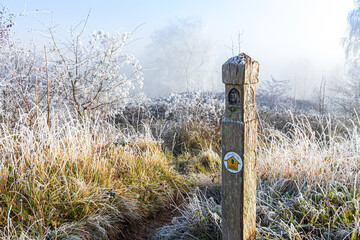 A Cotswold Way waymark post in hoar frost after a receding mist on Rudge Hill Nature Reserve...