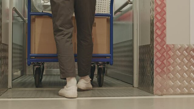 Low section following shot of legs of unrecognizable man with dolly cart leaving elevator and walking through corridor of self service storage