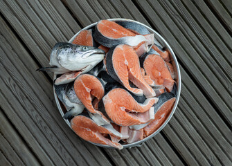 Metal baking tray filled with Large pieces of fresh raw atlantic salmon and Fresh salmon head. The protein is cut into steaks exposing the bright orange color of the fish with grey and black skin. Pre