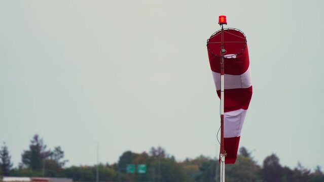 Striped white and red indicator installed on roof of general aviation airport building showing wind speed and direction to pilot operating airplane. Wind sock blows against in view blue sky