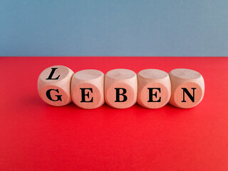 Turned a dice and changes the German word leben to geben (giving birth). Beautiful red table, blue background. Medical concept, copy space.