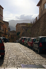 Narrow cobblestone street with densely parked cars. Typical Sicilian street with old residential houses. Underwear drying on the balcony fence. Concept of street parking in Castelbuono village, Sicily