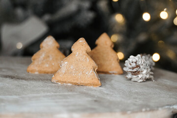 Close-up of Christmas tree biscuits on wooden table with out of focus lights in the background.