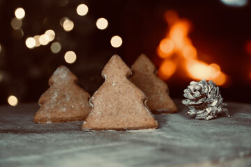Close-up of gingerbread biscuits in the shape of a Christmas tree with out-of-focus lights and a lit fireplace in the background.